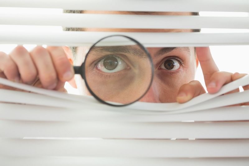 shot of a person looking through blinds with a magnifying glass