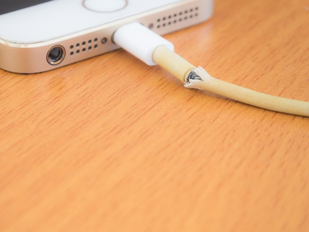 Close-up of a broken charger cable plugged into a smartphone, a defective product that can lead to low seller performance on Amazon