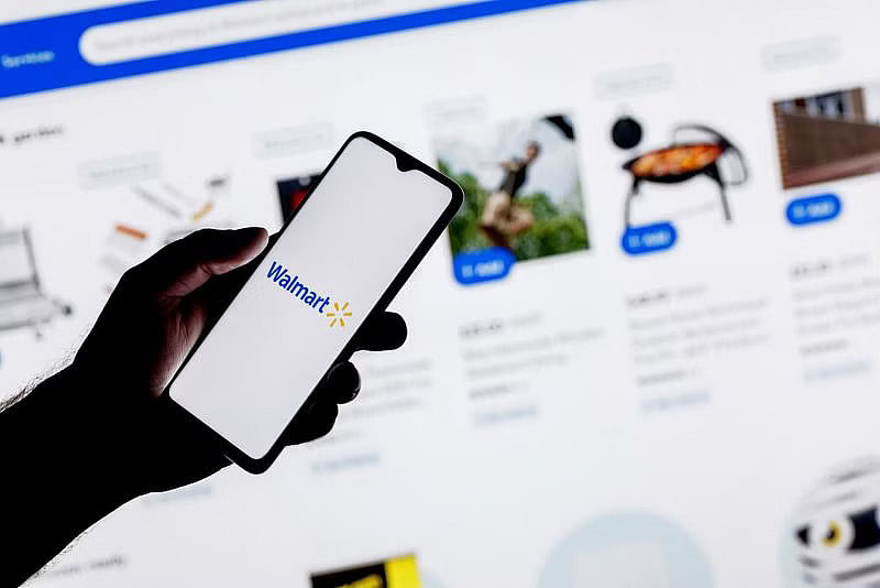 a hand holding a phone with walmart logo on the screen, against a backdrop of walmart product listings