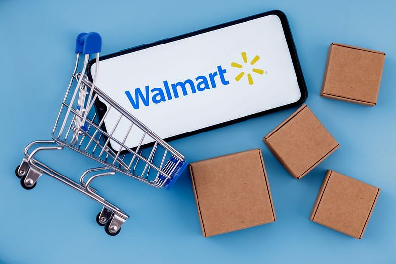 smartphone with Walmart logo on the screen surrounded by shopping cart and parcels