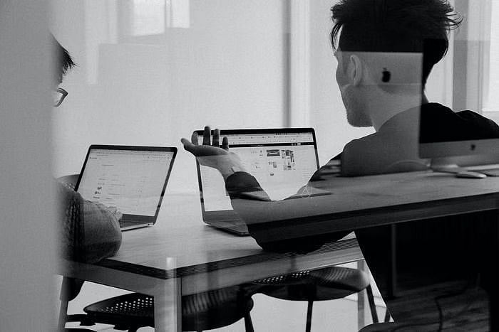 two men in black and white looking at laptops while discussing something