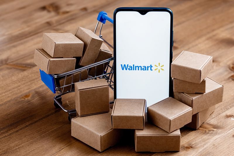 smartphone with Walmart logo on the screen surrounded by shopping cart and parcels