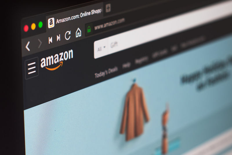 closeup of amazon website logo with blurred clothing products in the background