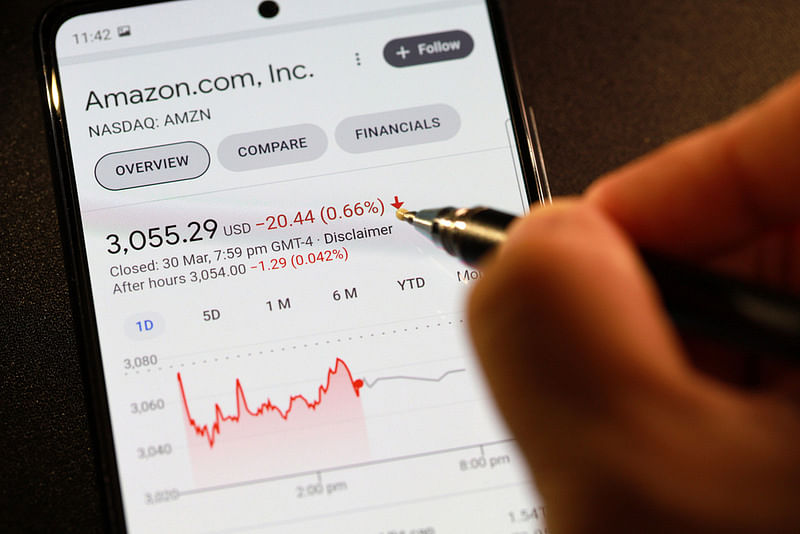 amazon nasdaq exchange on a mobile phone and a man holding a pen on the foreground