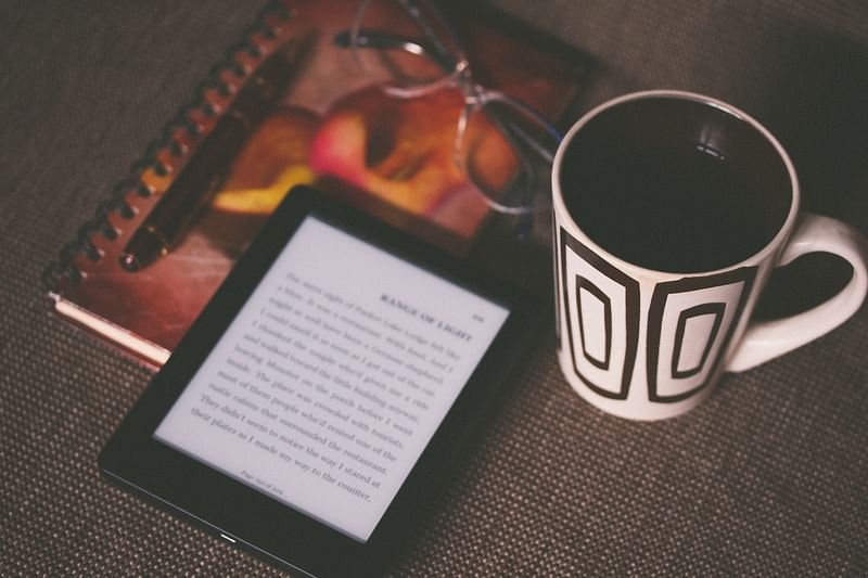 black E-book reader beside mug, glasses, pen, and notebook