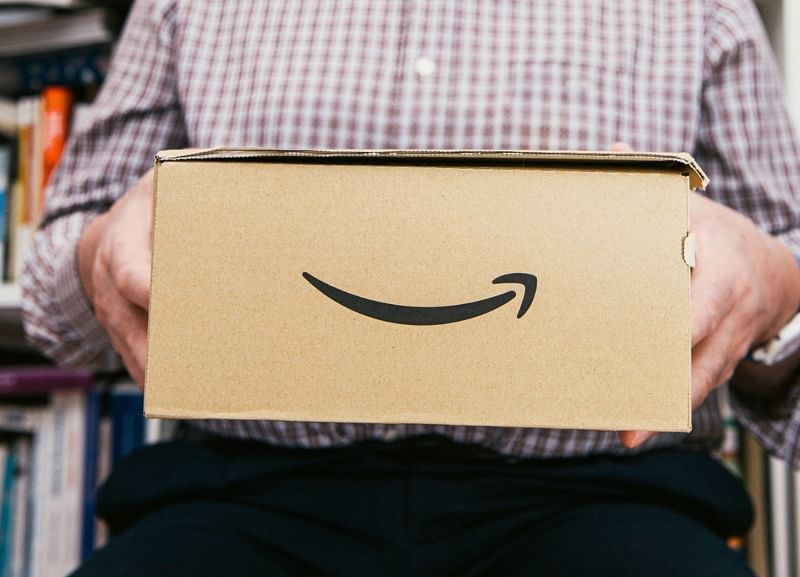 closeup shot of a person wearing long-sleeved plaid holding an amazon box with the amazon smiling logo on its side