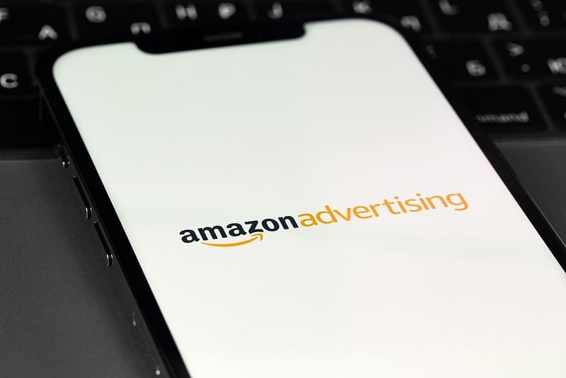 a mobile phone showing the Amazon Advertising logo with a laptop on the background
