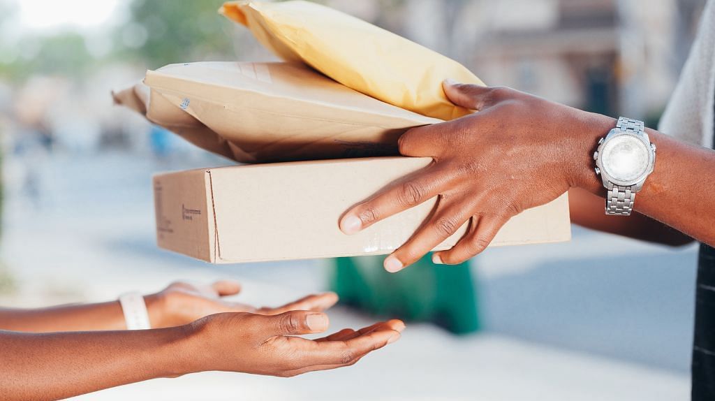 A delivery man with a watch on his left wrist handing over three packages to open hands