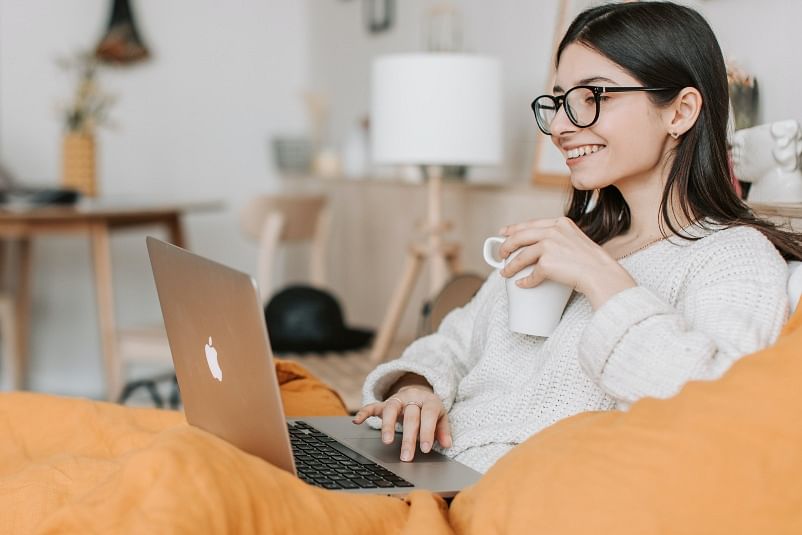shot of a lady holding a mug and smiling at her laptop